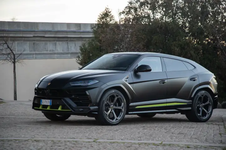 Un imponente **lamborghini urus negro** se exhibe con detalles en verde lima, posado sobre un camino empedrado.