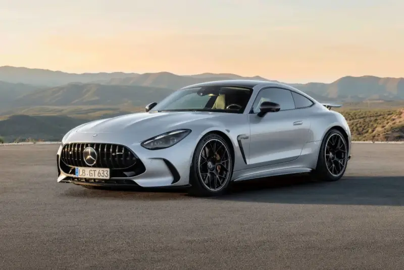 Un elegante Mercedes GTR plateado descansa en una carretera desierta, con montañas onduladas al atardecer de fondo.